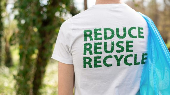 Man at plastic garbage collecting in a polluted park. Rubber gloves, carrying a bag with plastic bottles. Eco inscription on the T-shirt